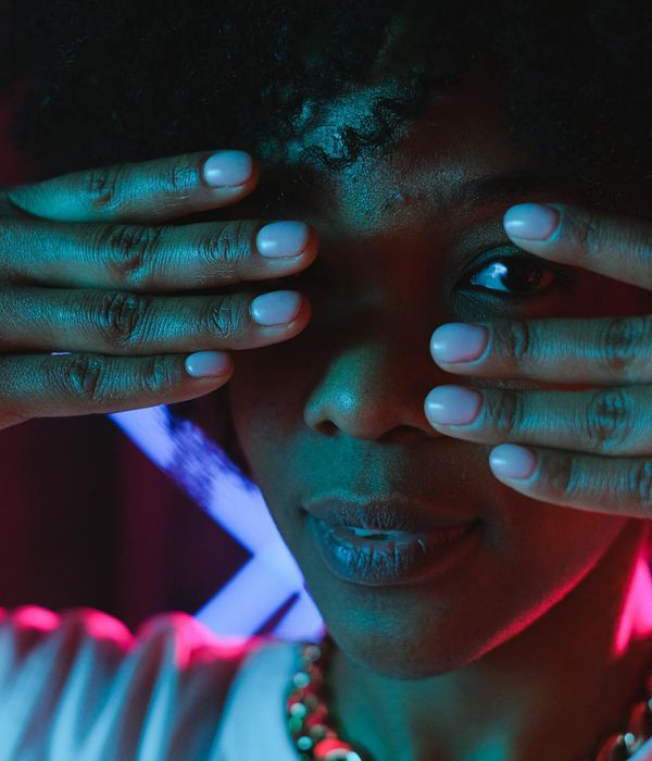 Woman in a calm, powerful pose against a dark background with pink light accents.